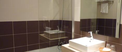 Un baño moderno con ducha envuelta en vidrio, un lavabo blanco y un espejo sobre él.