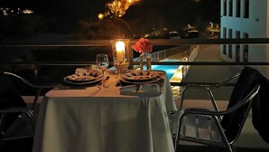 Mesa de comedor para dos con vista a un edificio iluminado y una piscina al fondo.