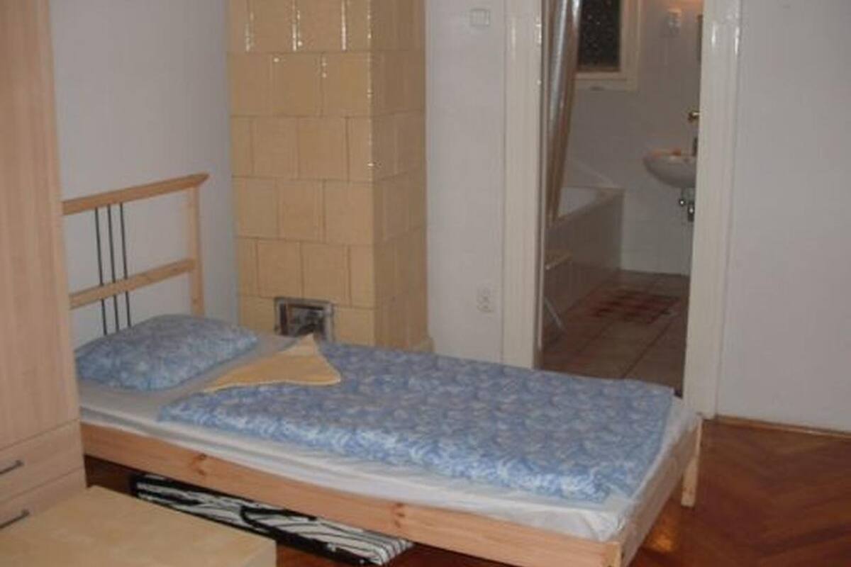 Un dormitorio pequeño con una cama individual, cabecera de madera, una mesita y un espejo.