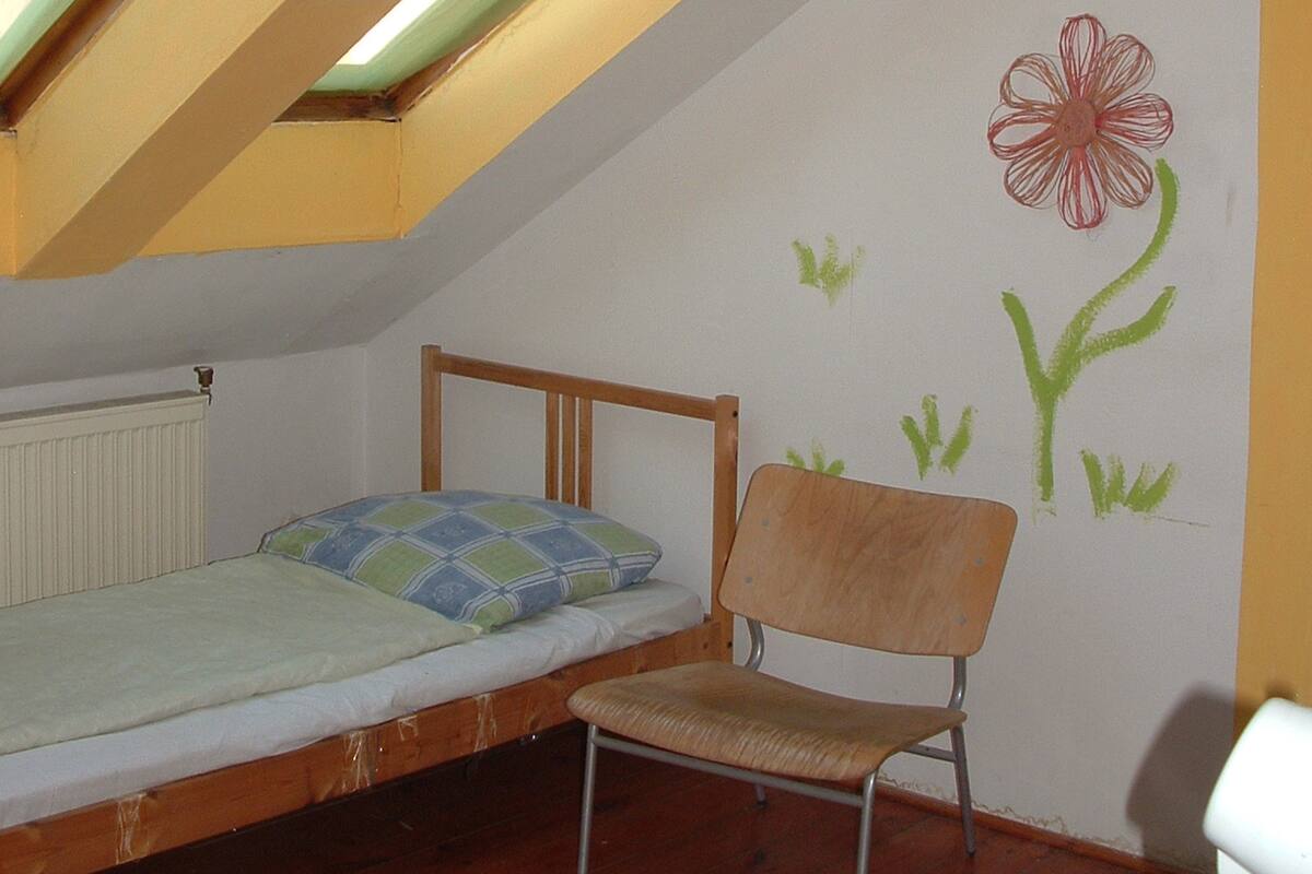 Un dormitorio con cama alta, una silla y tragaluz.