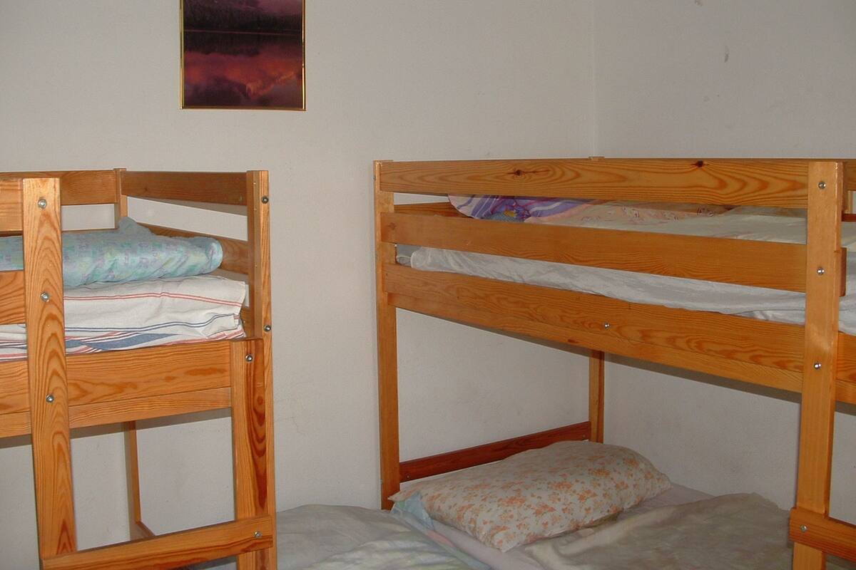 Dos literas con estructura de madera, una pared lisa y un cuadro enmarcado sobre la cama izquierda.