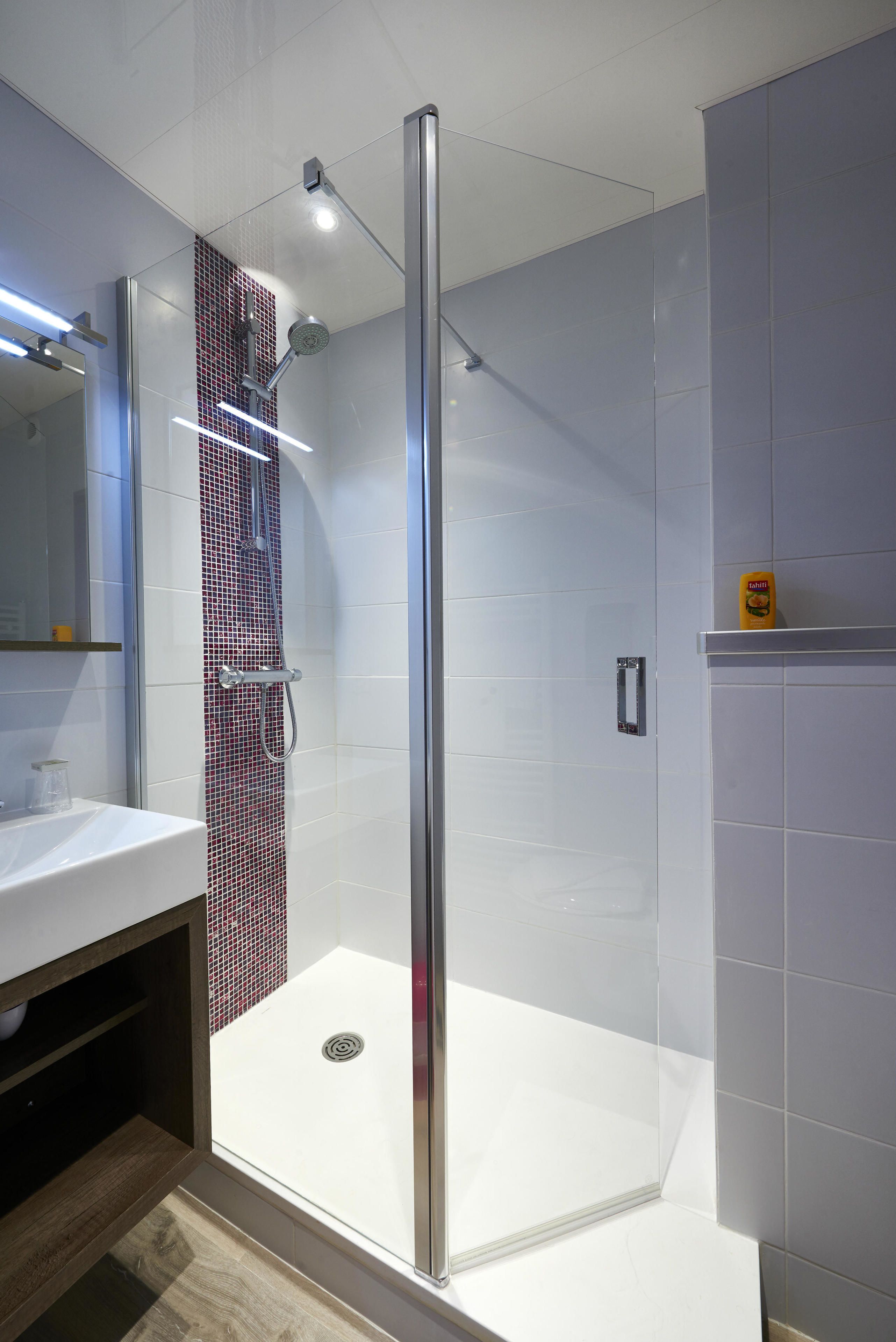 Une salle de bain moderne avec une douche à parois de verre, des carreaux blancs et un drain apparent.