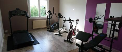 Uma academia em casa com esteira, bicicletas ergométricas, remo e aparelho de supino.