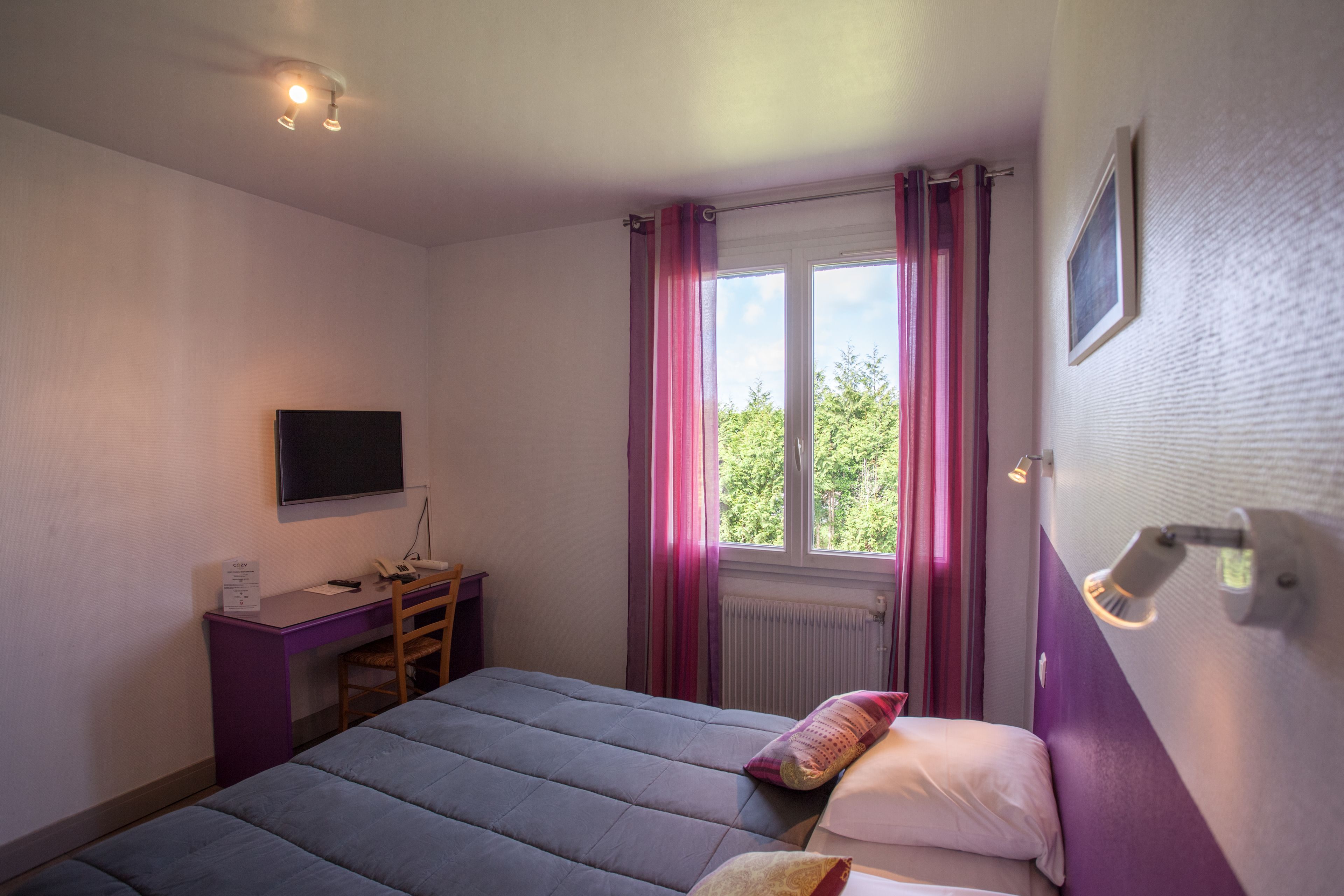 A bedroom with a bed, a desk, a chair, a TV, and a window with curtains.