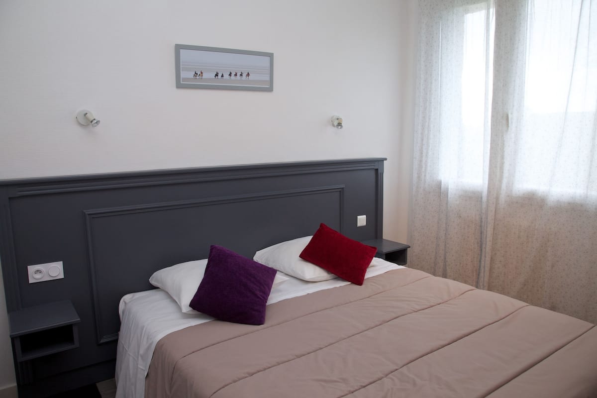 A neatly made bed with a headboard, two bedside tables, and a wall-mounted light switch.