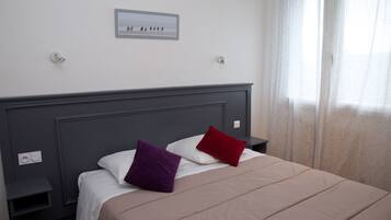 Una cama bien hecha con cabecera, dos mesitas de noche y un interruptor de luz en la pared.