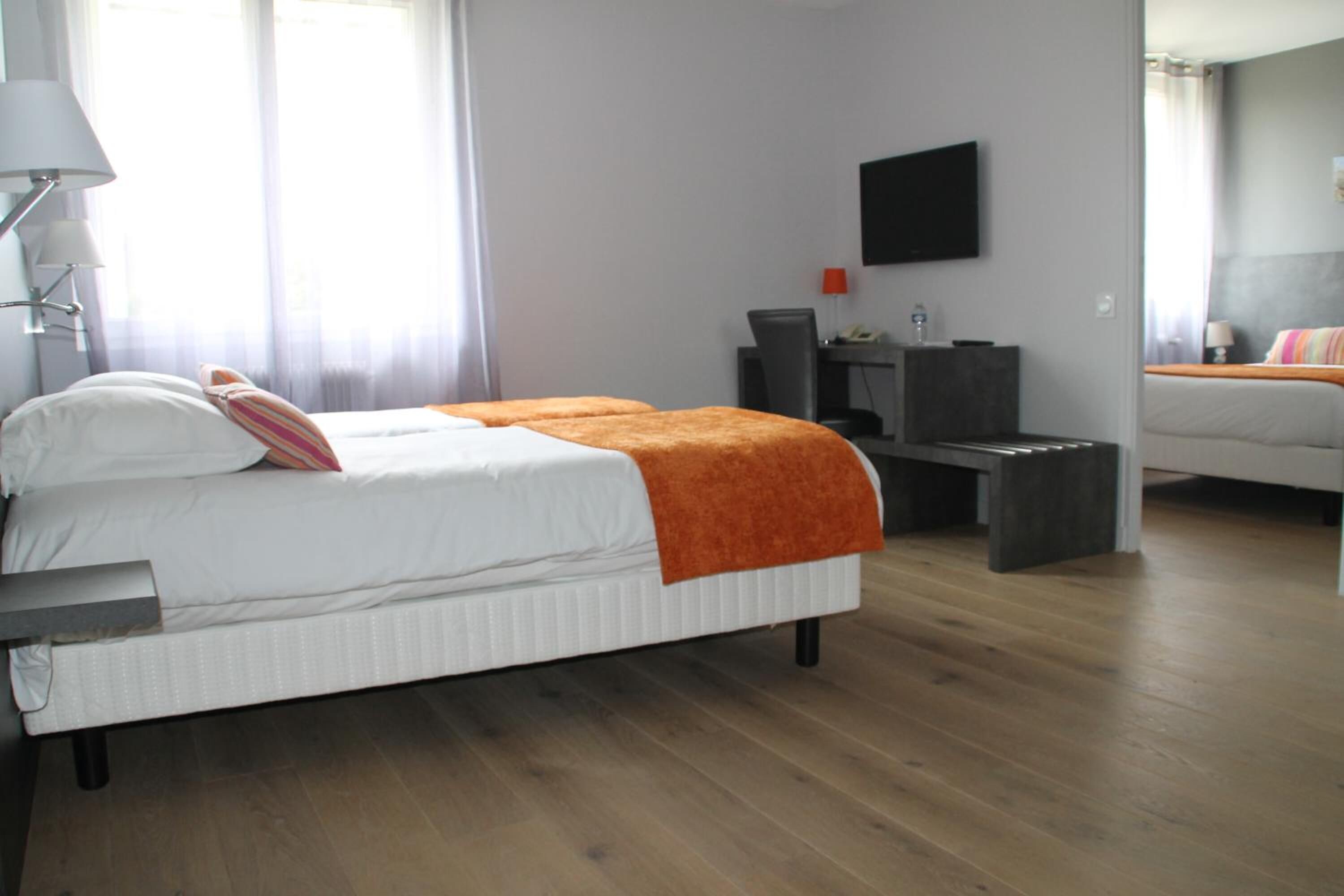 A modern hotel room with a large bed, a desk, a chair, a TV, and a sofa.