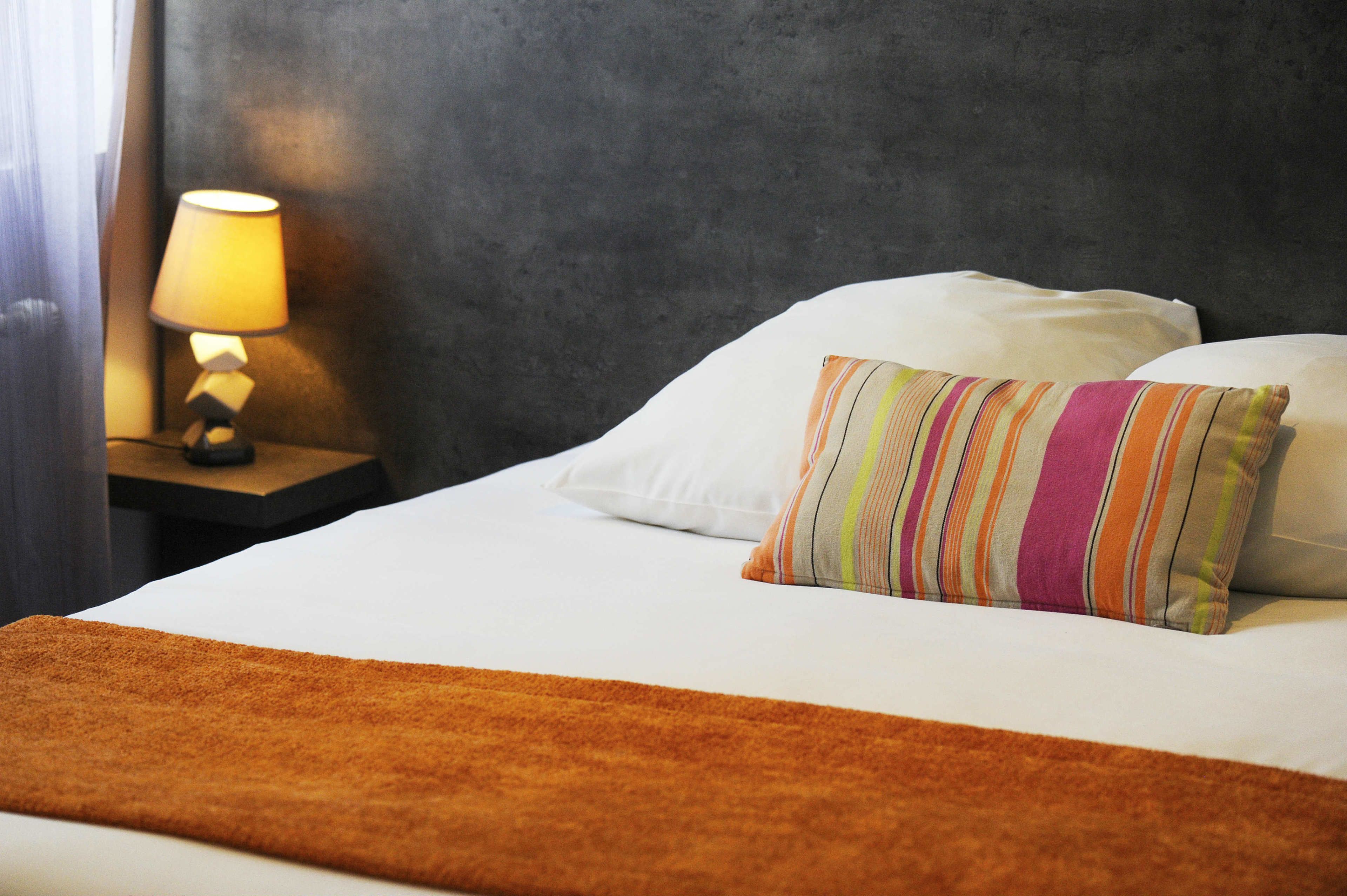 A hotel room with a bed, a nightstand with a lamp, and a striped pillow.