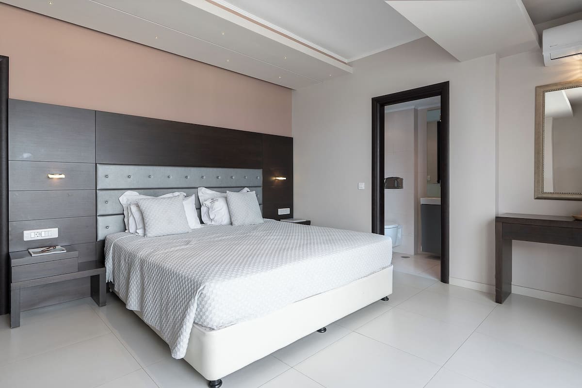 Ein modernes Schlafzimmer mit einem großen Bett, Nachttischen, einem Schminktisch und einer Tür zum Badezimmer.
