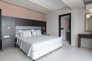A modern bedroom with a large bed, bedside tables, a nightstand, a mirror, and a door leading to a bathroom. - Kymothoe Elite Suites (Zakynthos)