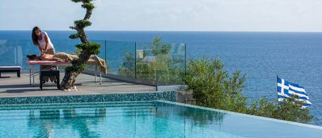 A pool with a view of the sea, a person lying on a lounge chair, and a flag.