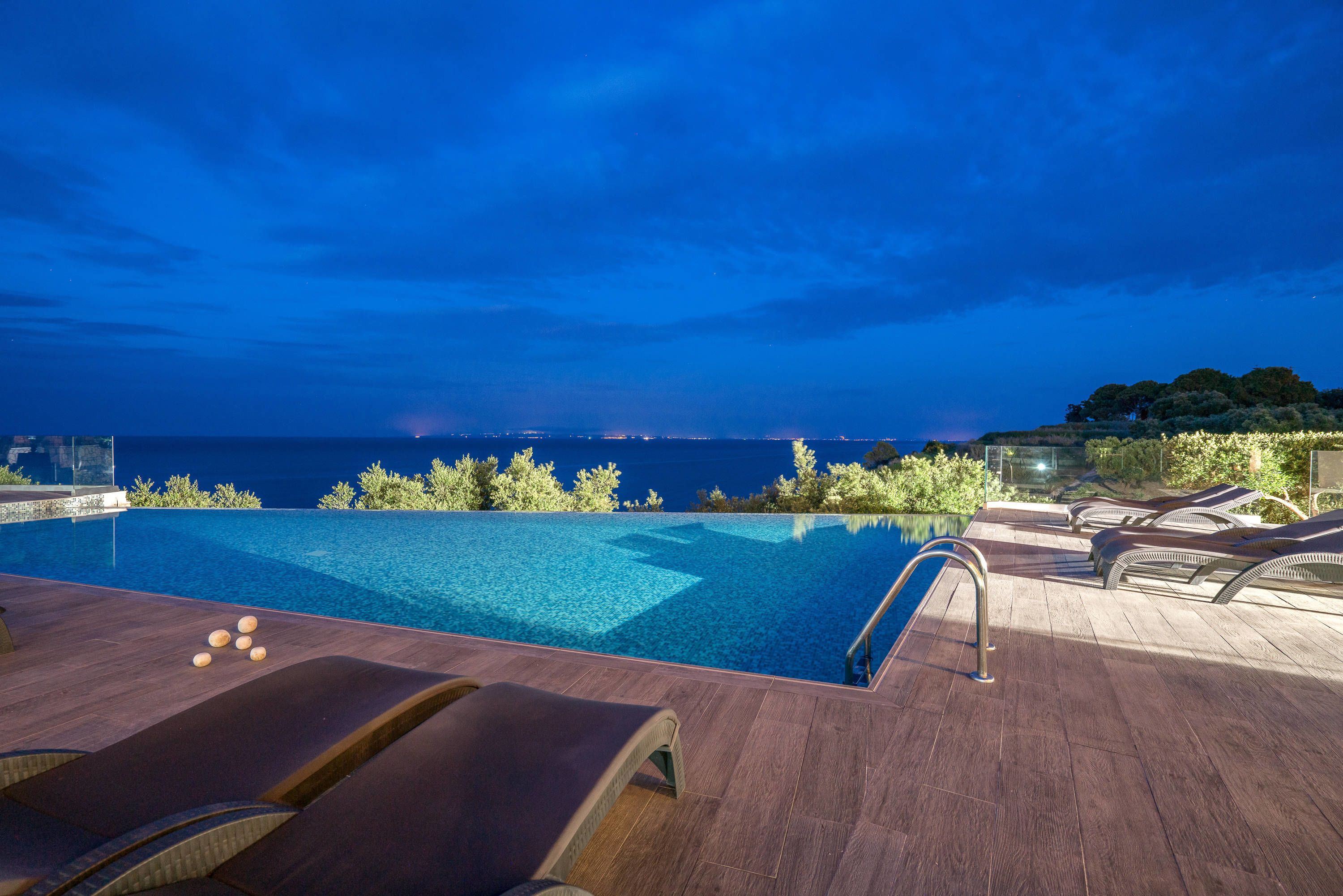 A poolside area with lounge chairs and a view of the sea at dusk.