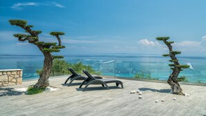Una terraza con dos sillones de relax con vista a un mar azul y una barandilla de cristal.