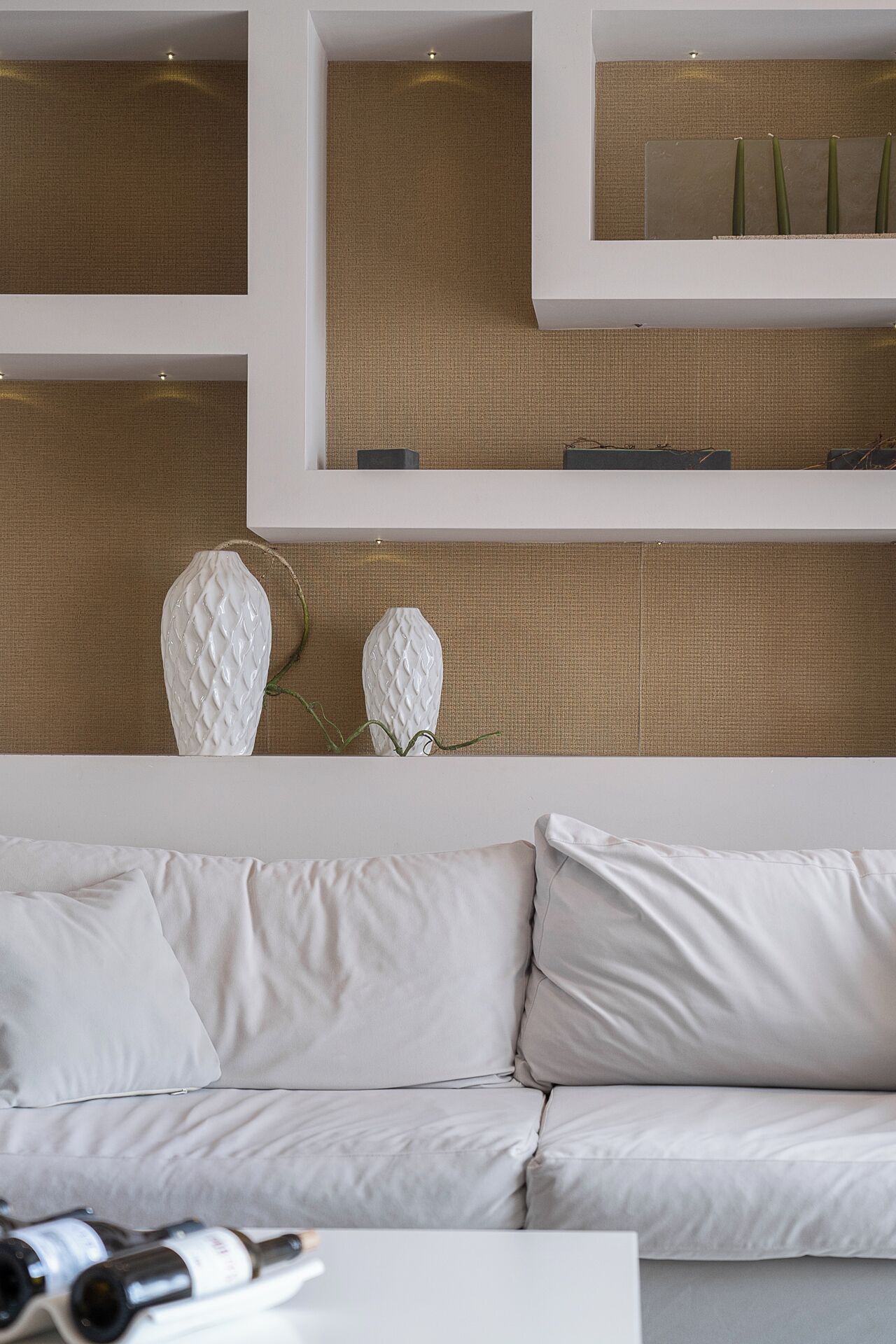 A modern living room with a white sofa, decorative vases, and a wine rack.