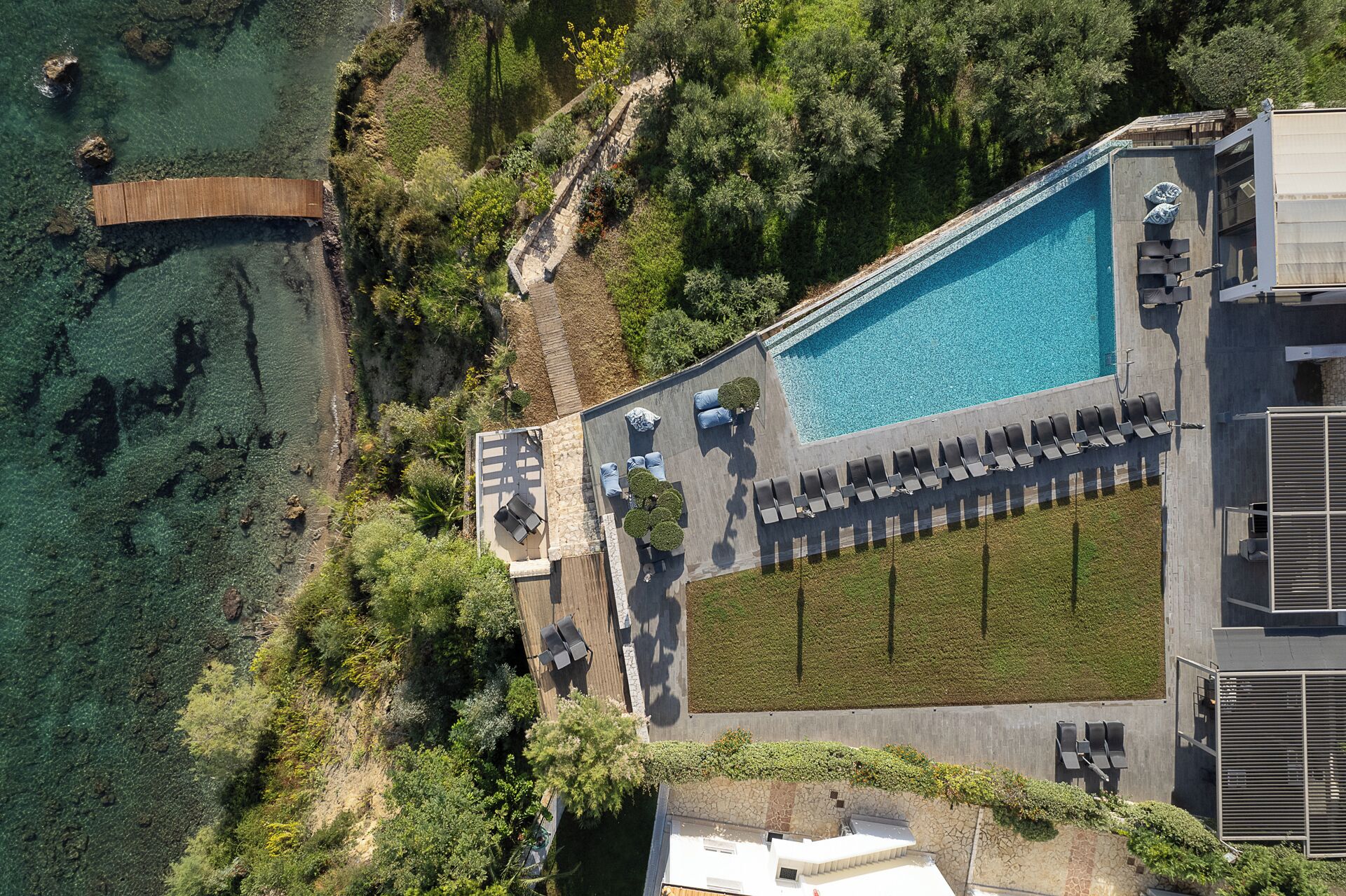 An aerial view of a resort with a swimming pool, lounge area, and surrounding greenery.