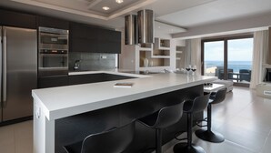Una cocina moderna con una isla central, taburetes de bar y vistas al mar a través de amplios ventanales.
