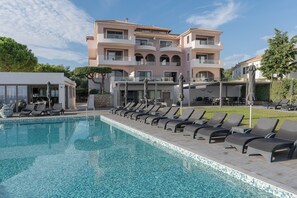 A swimming pool with lounge chairs, a building with balconies, and a clear sky. - Kymothoe Elite Suites (Zakynthos)
