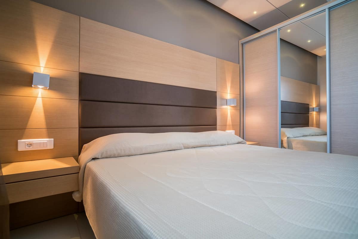 Ein modernes Schlafzimmer mit einem großen Bett, Nachttischen und einem Kleiderschrank mit Spiegel.