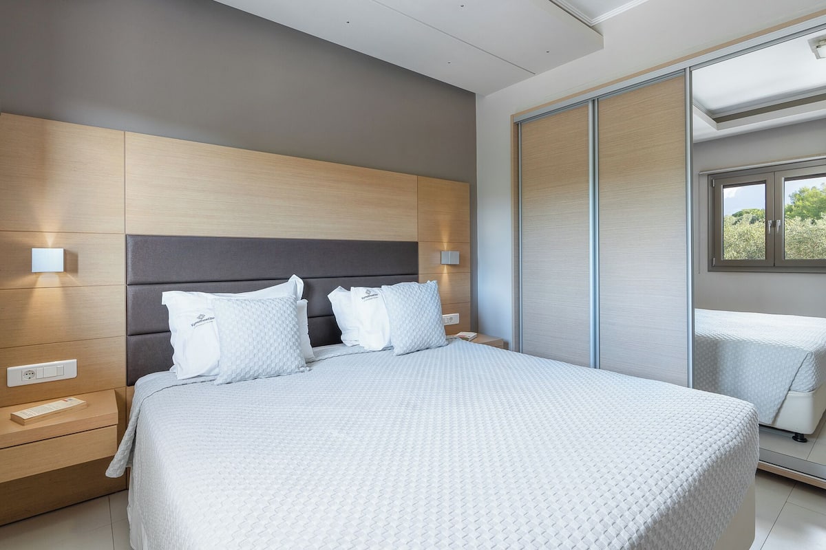 Ein modernes Schlafzimmer mit einem großen Bett, einem Nachttisch, einer Wandleuchte und einer Schiebetür, die auf einen Balkon führt.