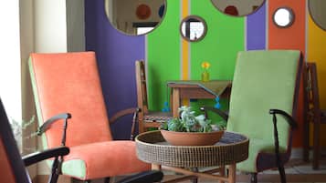 Una habitación con dos sillas, una naranja y otra verde, y una pequeña mesa con una planta en maceta.