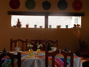 A dining area with a brick wall, a window with potted plants, and a table set with white cups and vases. - Munay La Quiaca (La Quiaca)