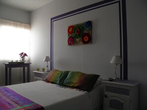 A bedroom with a bed, a nightstand, a table with a lamp, and a wall art piece. - Munay La Quiaca (La Quiaca)