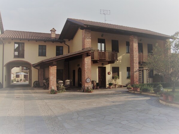 A two-story building with a brick facade, a balcony, and a courtyard with potted plants. - Al Calar della Sera (Sommariva del Bosco)
