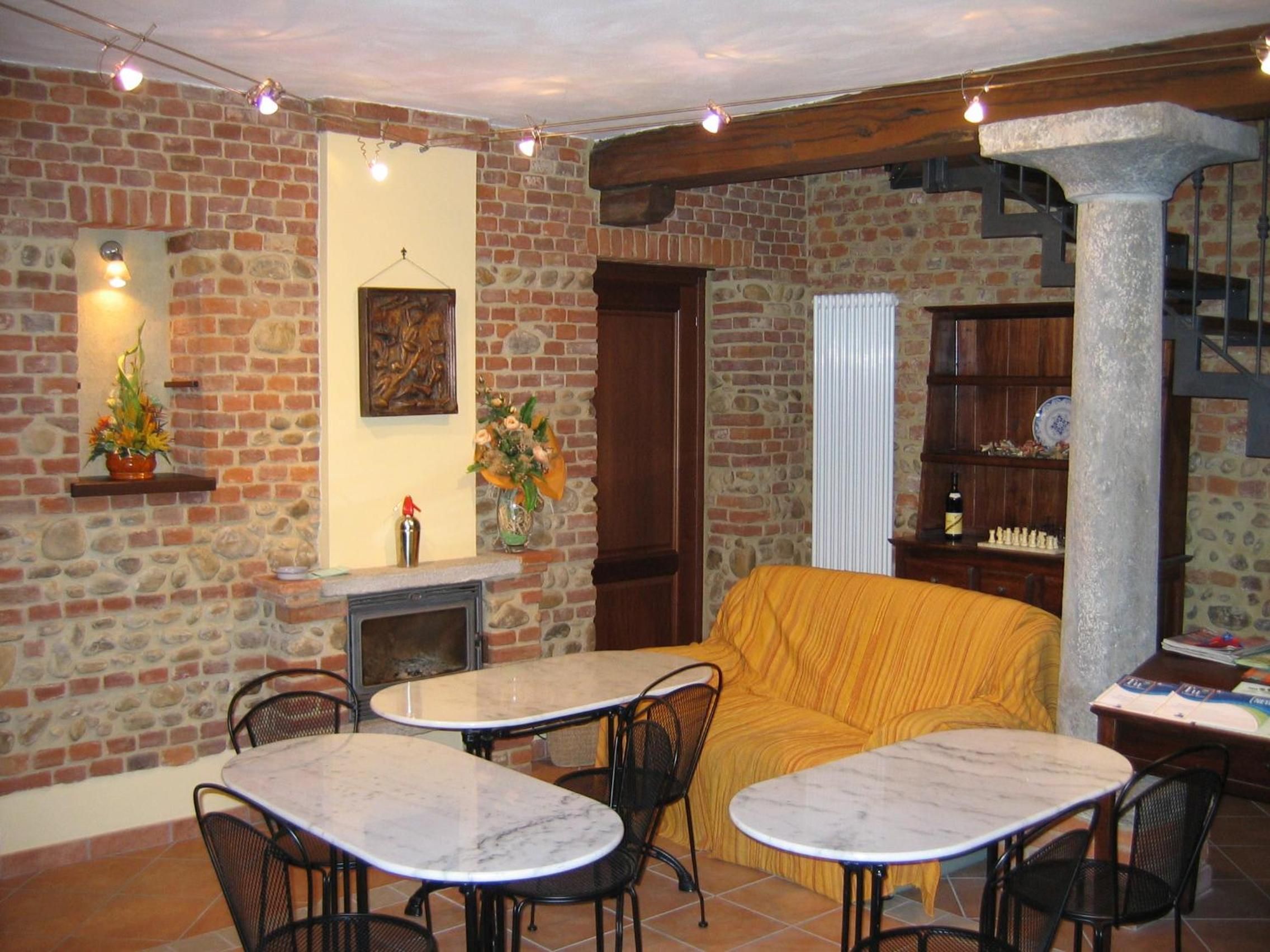 A cozy interior with a stone wall, a fireplace, a sofa, and a dining area with tables and chairs.