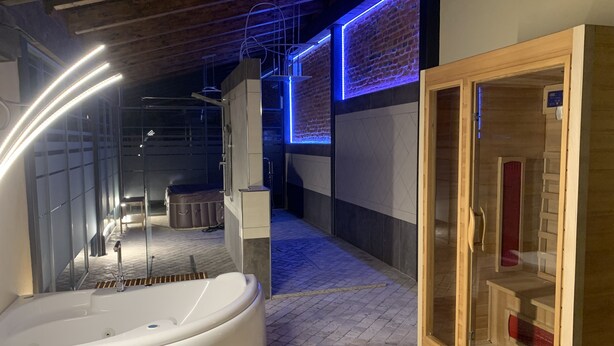 A spa area with a large white hot tub, wooden sauna, and a brick wall with blue lighting. - Al Calar della Sera (Sommariva del Bosco)