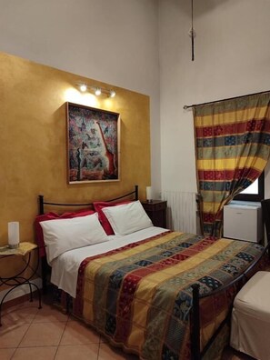 Une chambre à coucher comprenant un lit, une table de chevet, une commode, une fenêtre avec un rideau et un tableau accroché au mur.