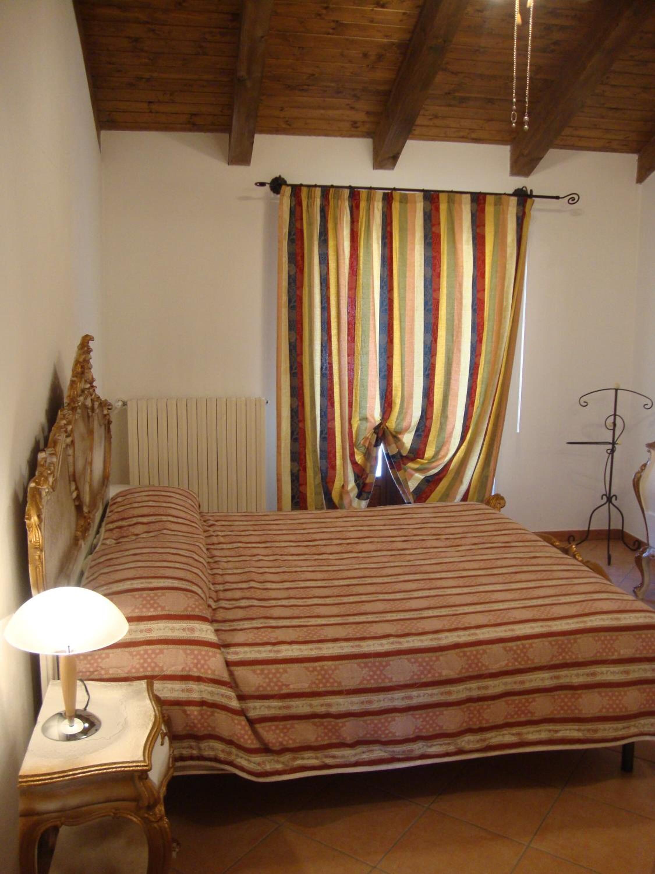 A bedroom with a bed, a nightstand, a lamp, a radiator, and a curtain.