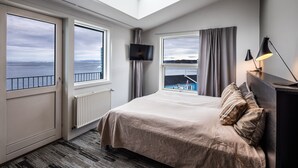 A bedroom with a bed, a TV, and large windows with a view of the sea. - Hotel Icefiord (Ilulissat)
