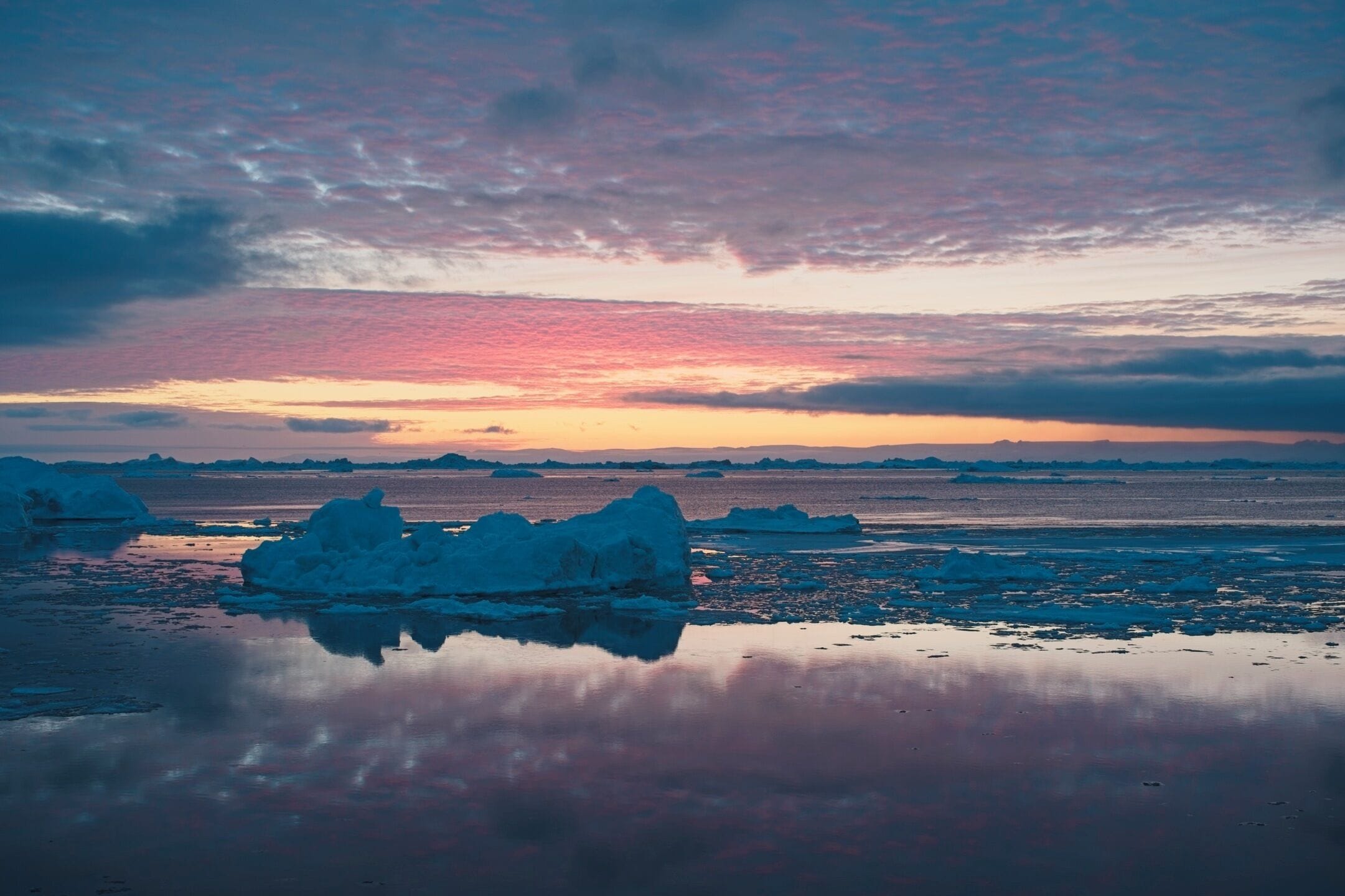 Una masa de agua tranquila con icebergs y un cielo al atardecer.