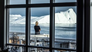 A person standing by a window overlooking a snowy landscape with icebergs. - Hotel Icefiord (Ilulissat)
