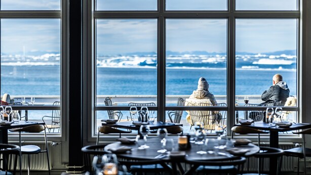A restaurant with large windows offering a view of the sea and distant land. - Hotel Icefiord (Ilulissat)