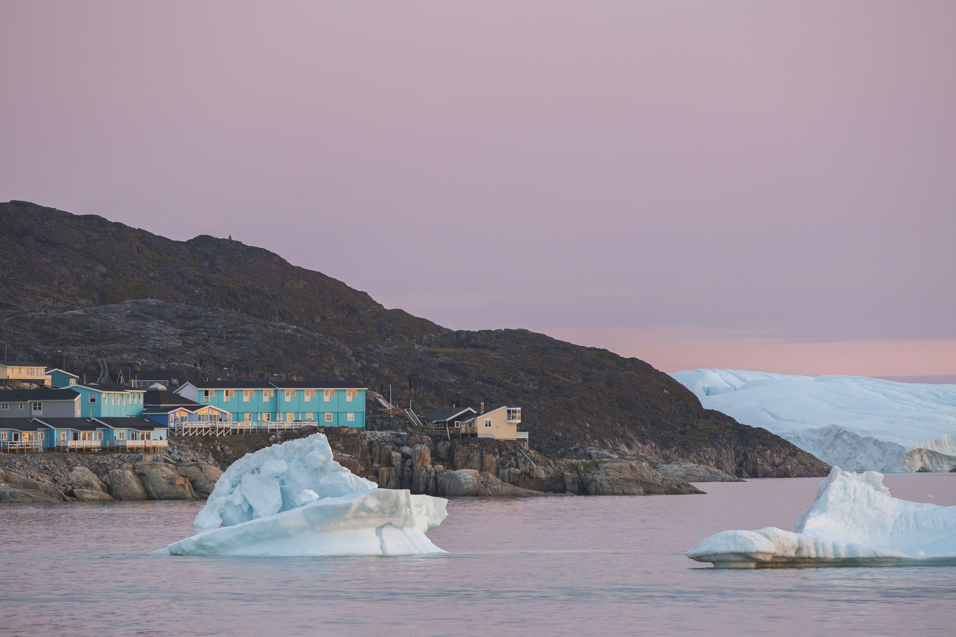 A coastal building with multiple rooms, situated near a glacier and icebergs.