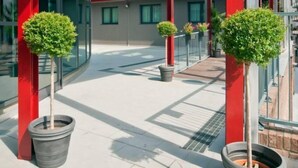 A modern building with red structural columns, a covered walkway, and potted plants. - Residenze Romeo e Giulietta  (Parma)