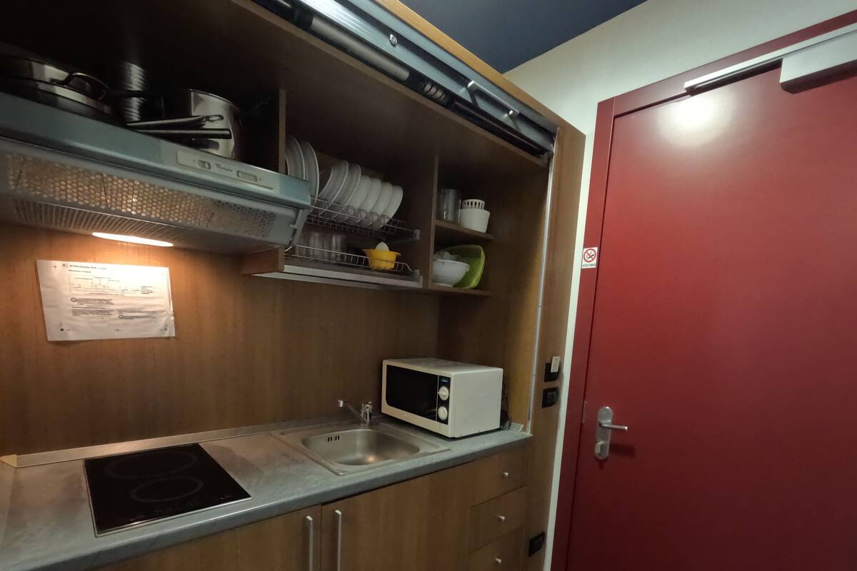 A compact kitchenette with a microwave, sink, and stainless steel range hood.