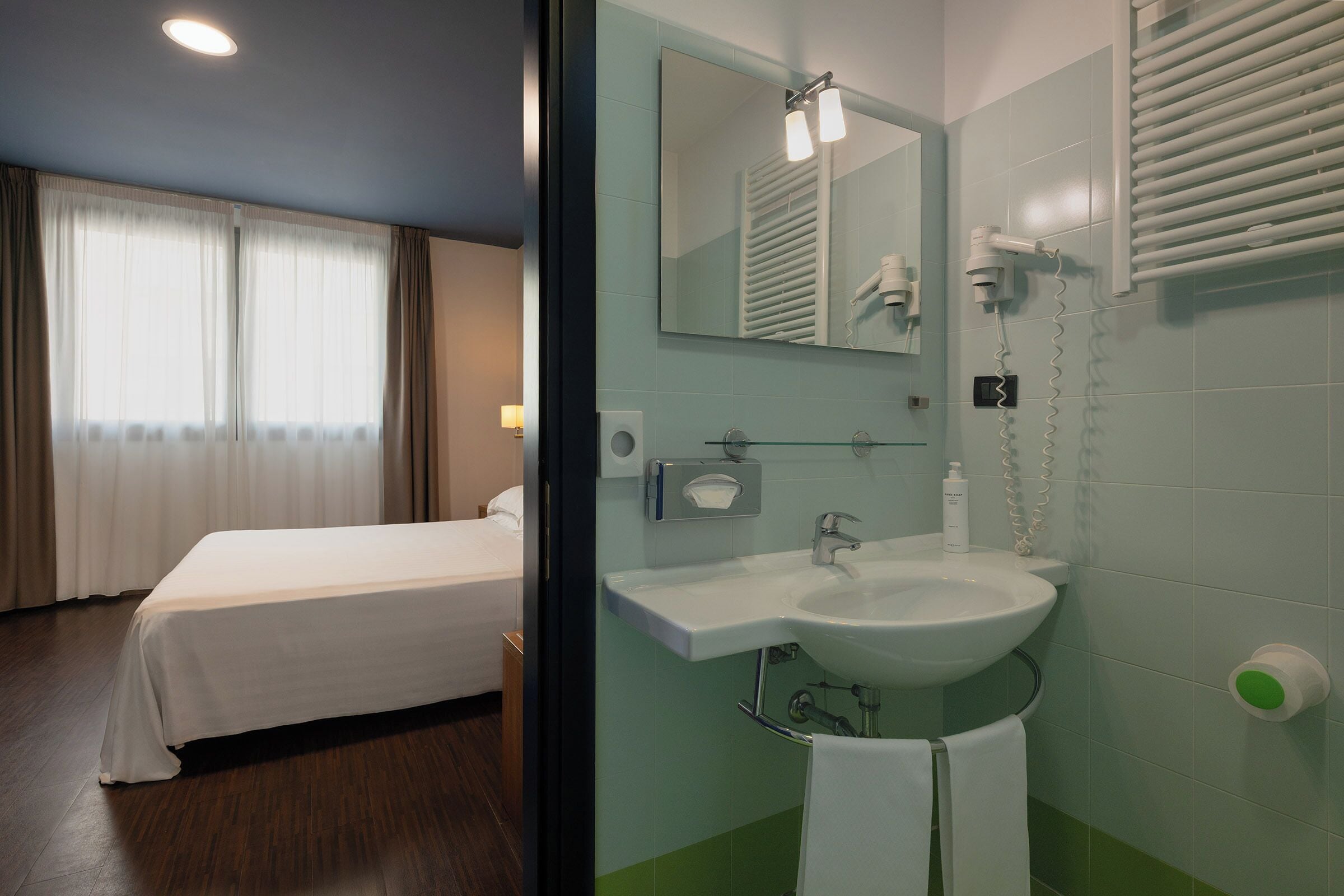 A hotel room with a bed, a bathroom with a sink, mirror, and towel rack.
