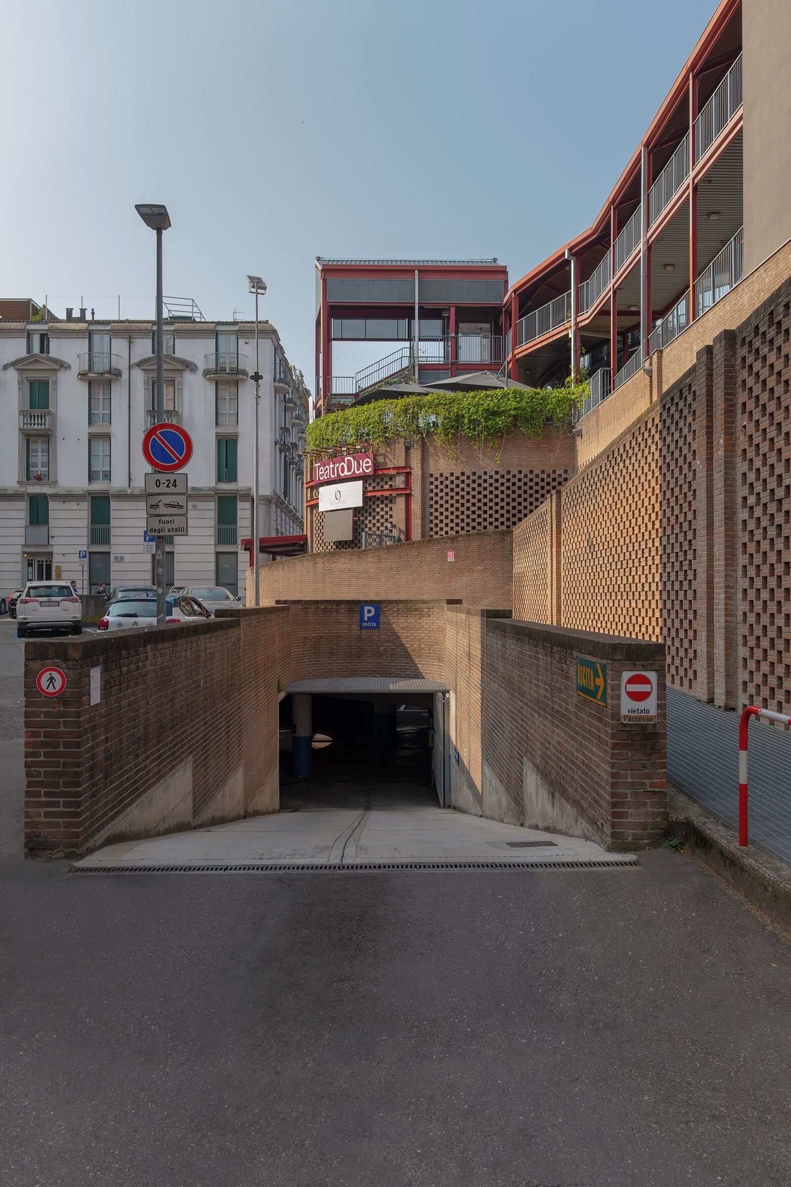 A building with a red-brick facade, a sign for Teatro Due, and a parking area with a blue sign indicating a parking space.