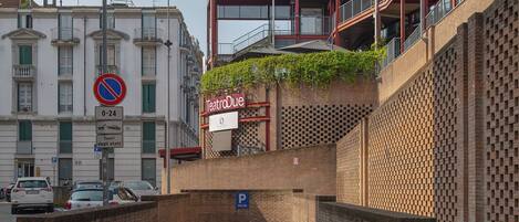 A building with a red-brick facade, a sign for Teatro Due, and a parking area with a blue sign indicating a parking space.