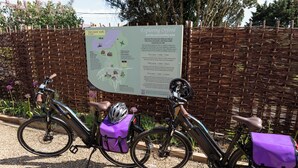 Un vélo avec un sac et un casque violets, garé devant un panneau indicateur.