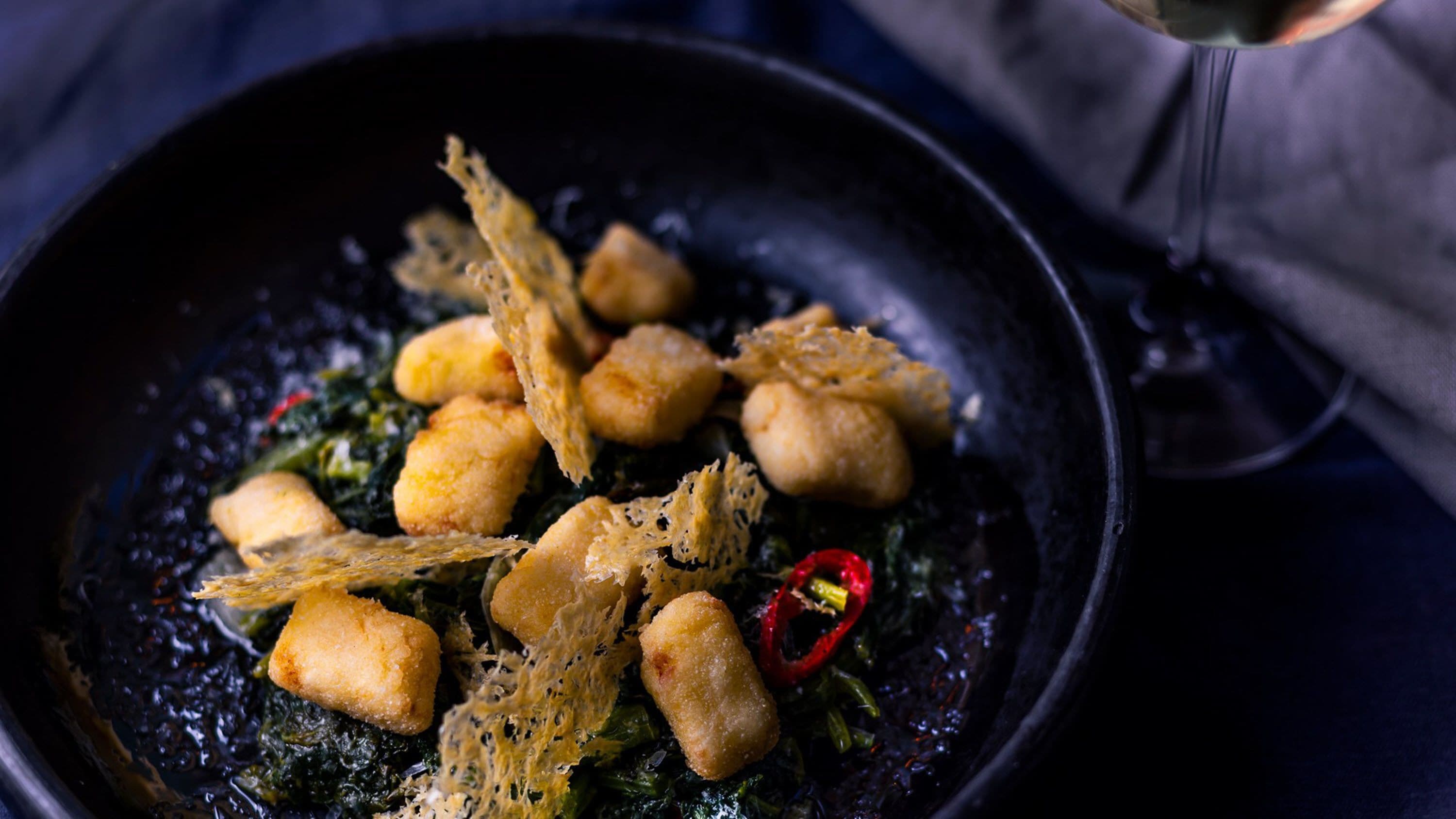 A dish with crispy fried items and greens in a black bowl.