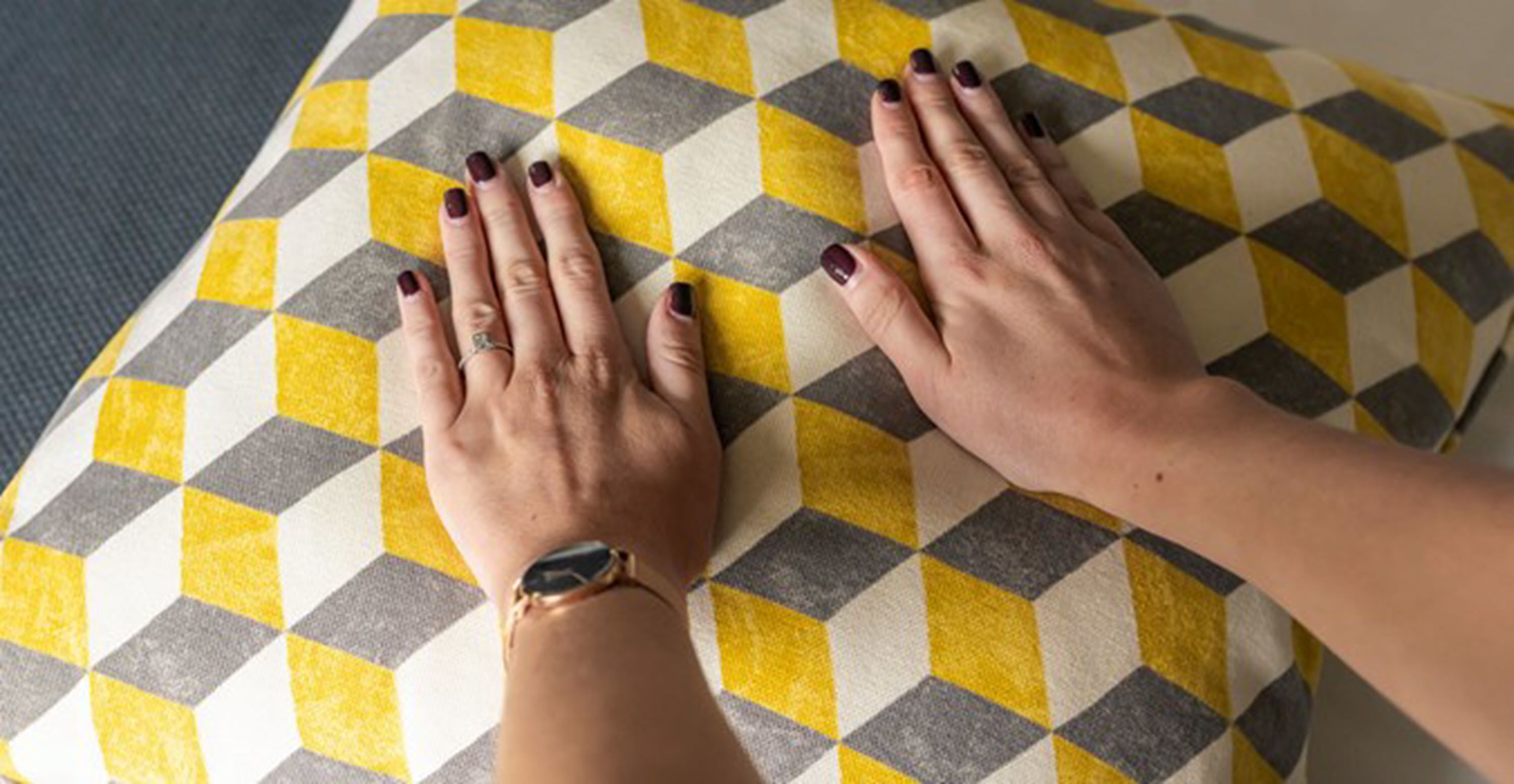 Une paire de mains reposant sur un coussin à carreaux avec un motif géométrique.