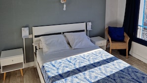 A bedroom with a bed, nightstands, a chair, and a window with curtains. - Hôtel Restaurant le Palais (Apt)