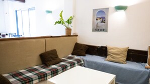 A cozy seating area with a sofa, a bench, and a small table. There is a potted plant on the bench and a poster on the wall. - Hôtel Restaurant le Palais (Apt)