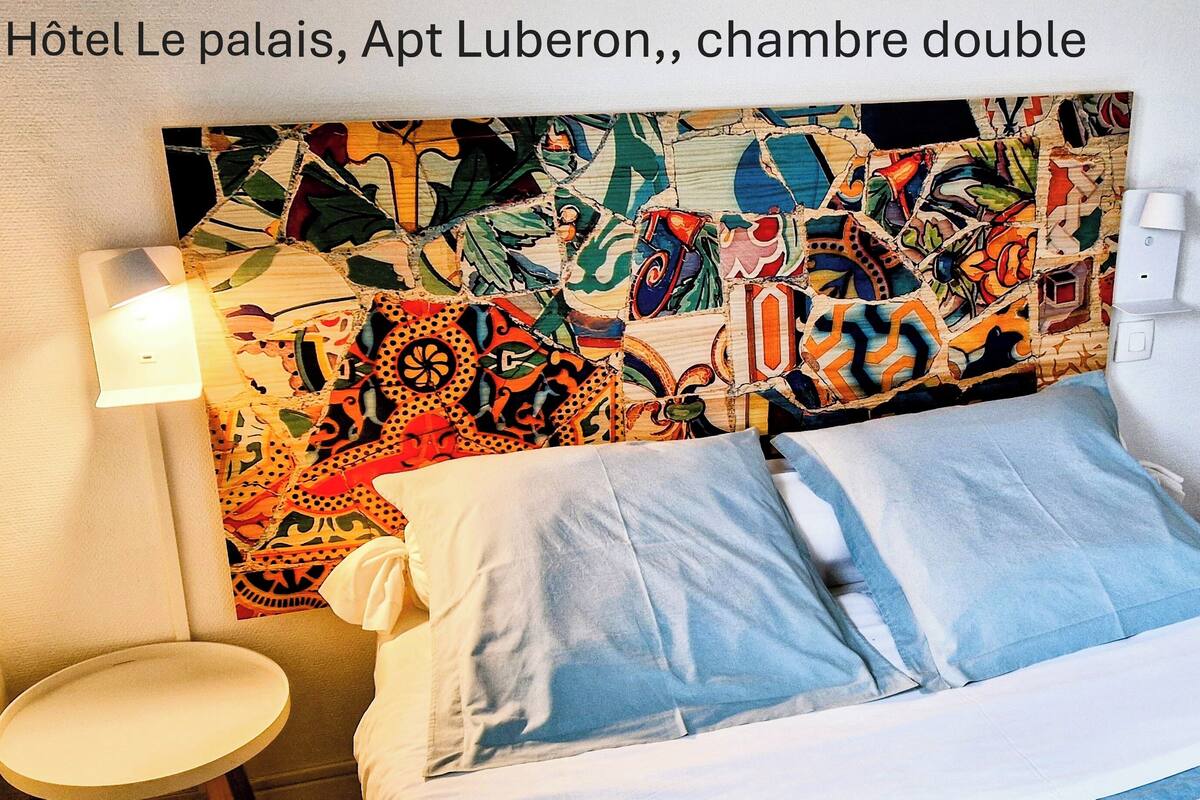 A double room with a colorful abstract headboard, a bedside table, and a chair.