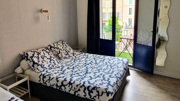Un dormitorio con cama, mesita de noche, ventana con cortinas y vista al balcón exterior.