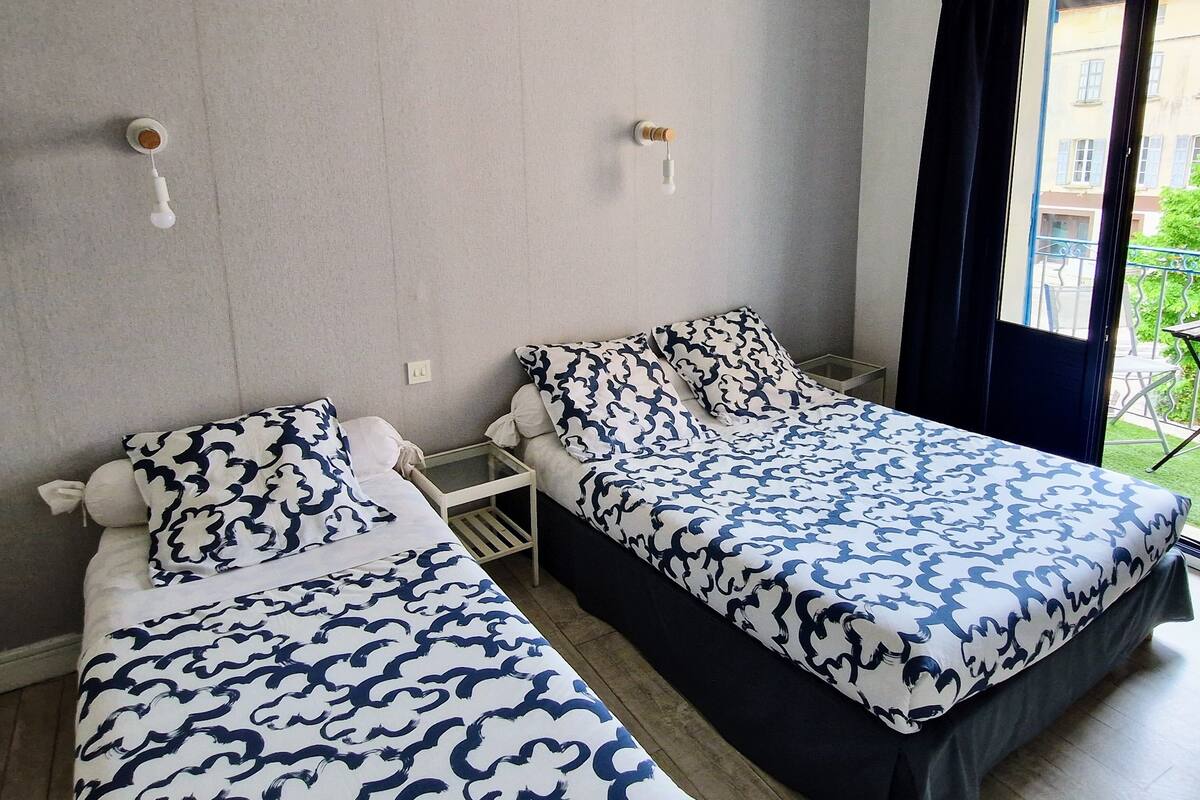 A hotel room with two beds, each with a patterned bedspread, a small table, and a window with a view of the outside.