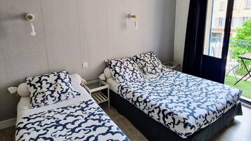 A hotel room with two beds, each with a patterned bedspread, a small table, and a window with a view of the outside.